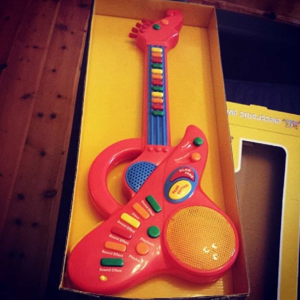 A red toy guitar is sitting in a box.
