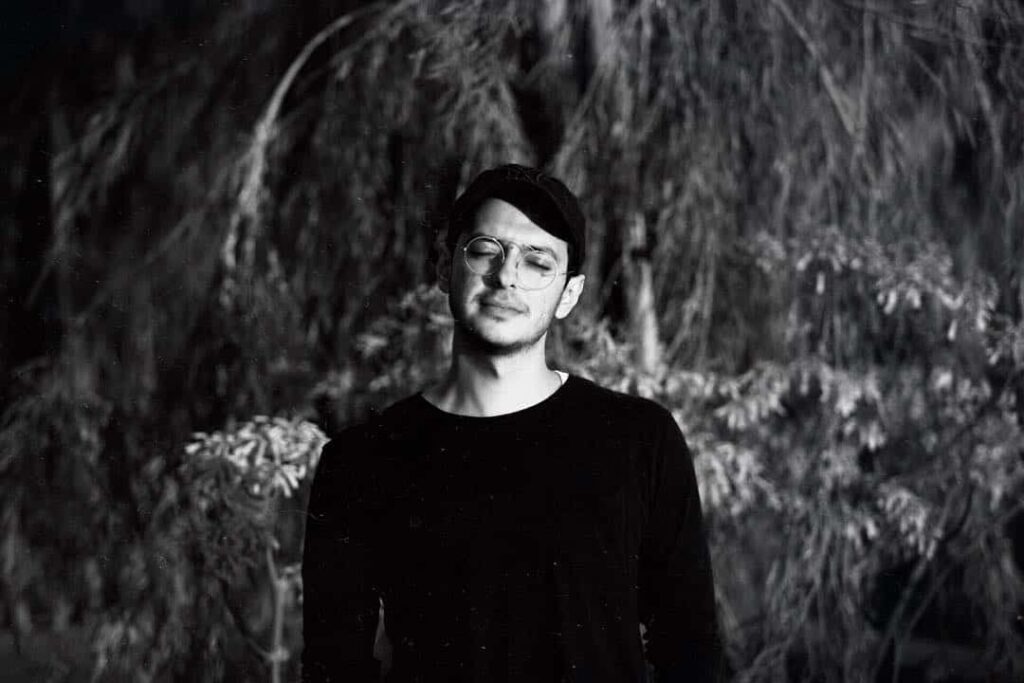 A black and white photo of a man standing in front of trees, possibly taken during an interview with RAMI.