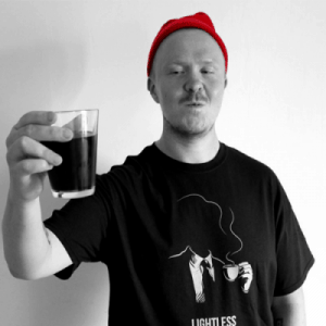 A man with a red beanie holding up a glass of coffee.