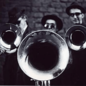 A black and white photo of a group of men playing trombones with infectious funk.