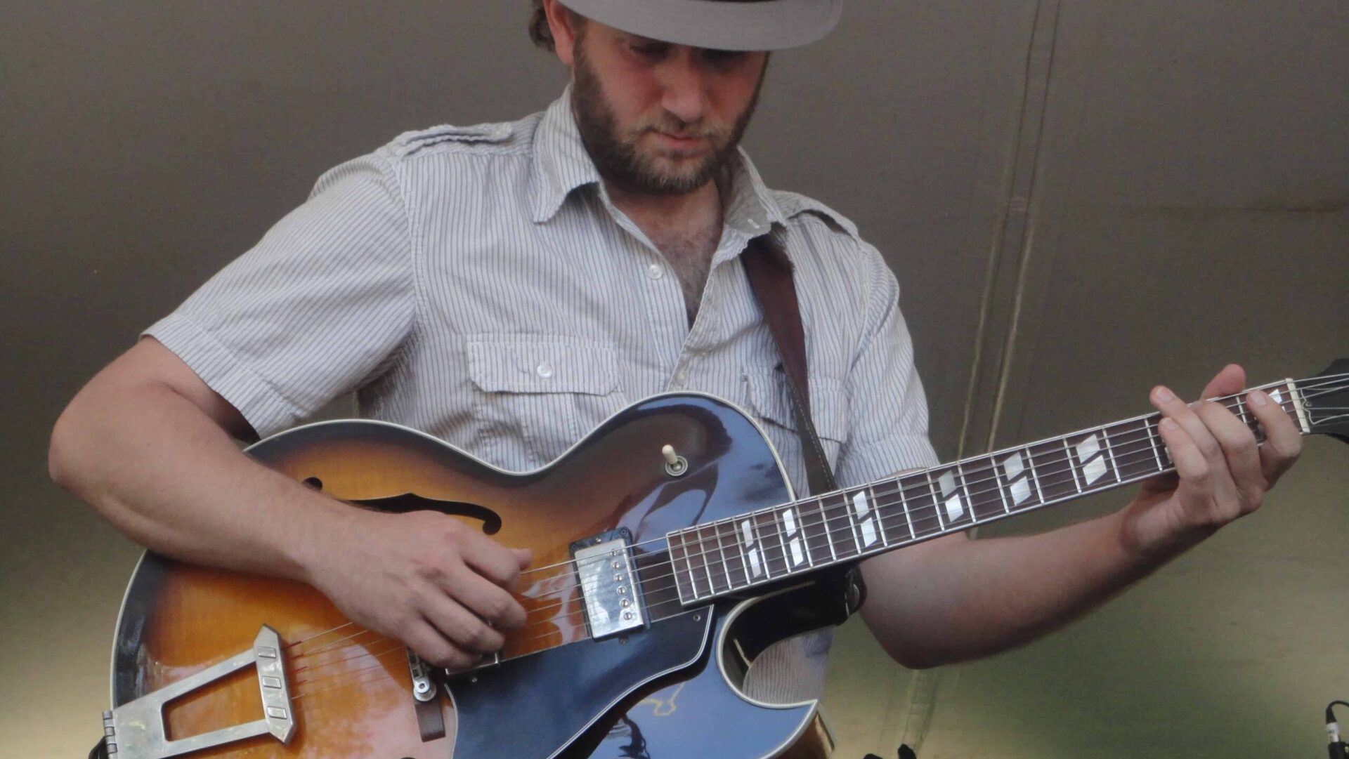 A quirky man in a hat playing a jazzy electric guitar.