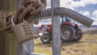 A gated padlock on a sidechained gate with a tractor in the background.