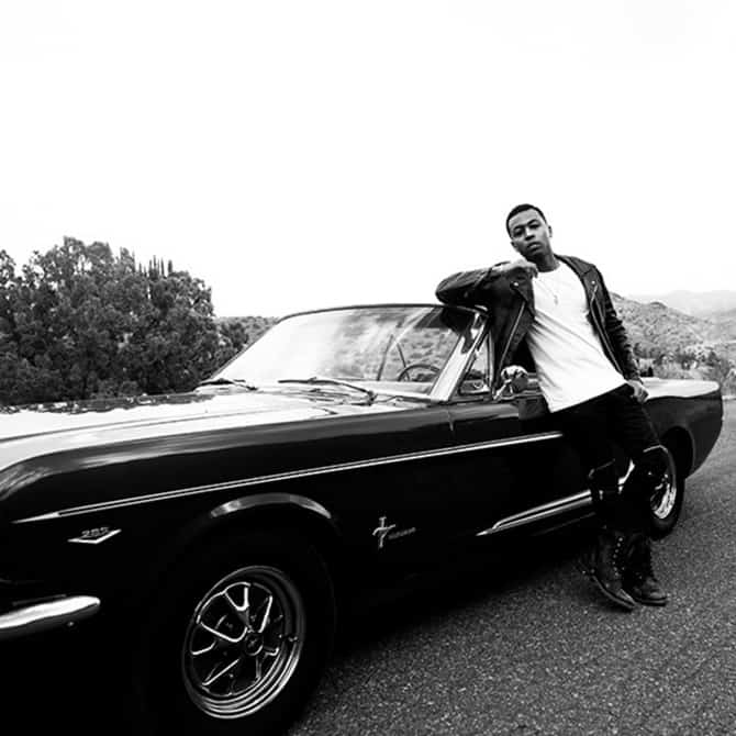 A black and white photo of Kevin Ross leaning on a classic car.