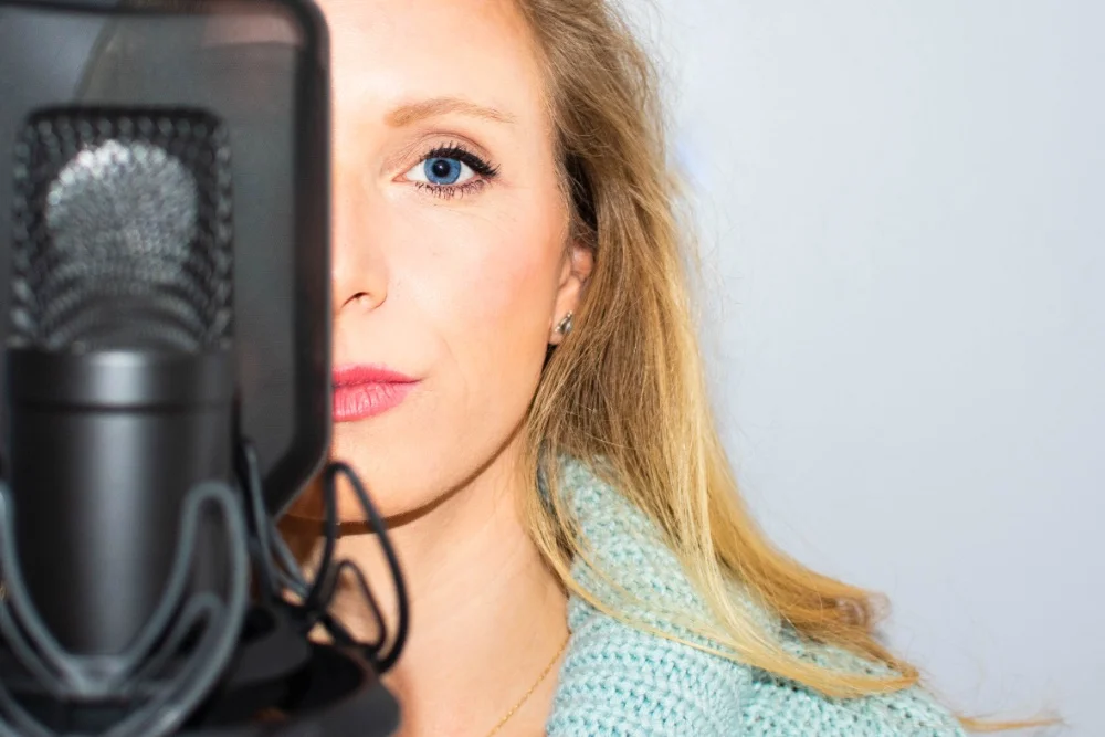 A woman with blue eyes is standing in front of a microphone, delivering her Nasal Vocals.