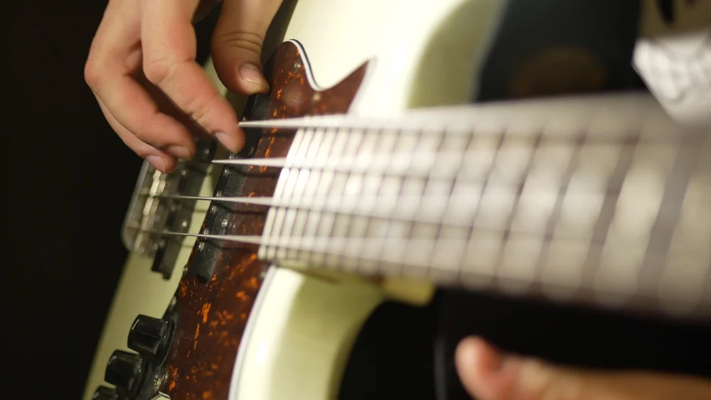 Close up of a person playing a bass guitar with Perfect Sound.