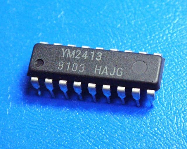 A small YM2413 electronic chip on a blue surface.