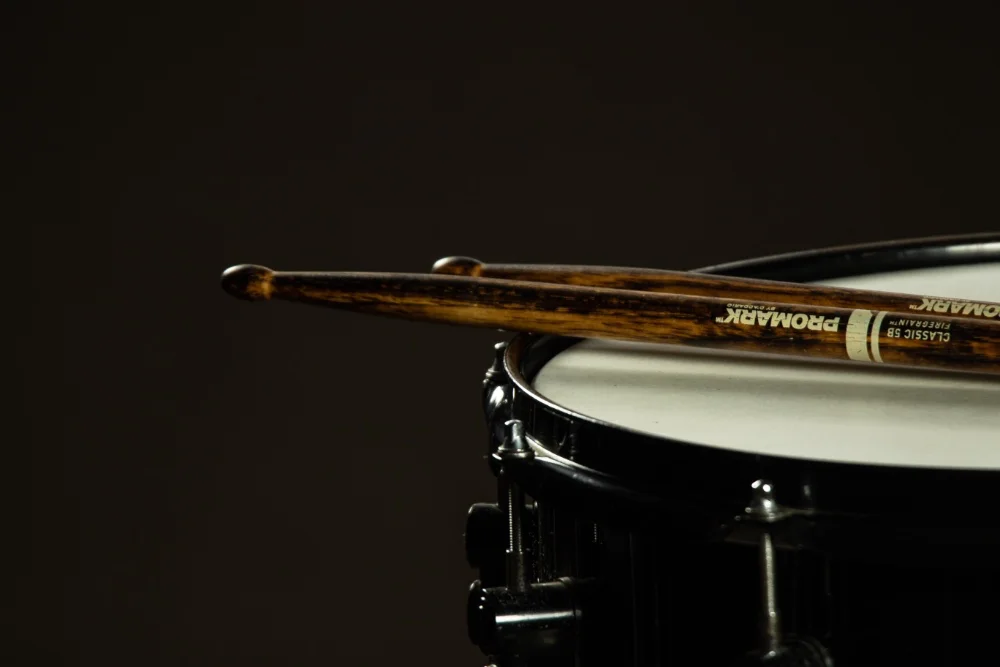 Photo of a snare drum and drumsticks on a dark background.