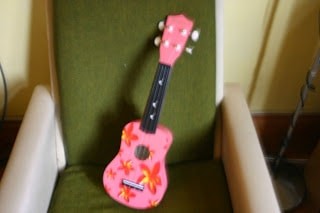 A pink ukulele resting on a green chair.