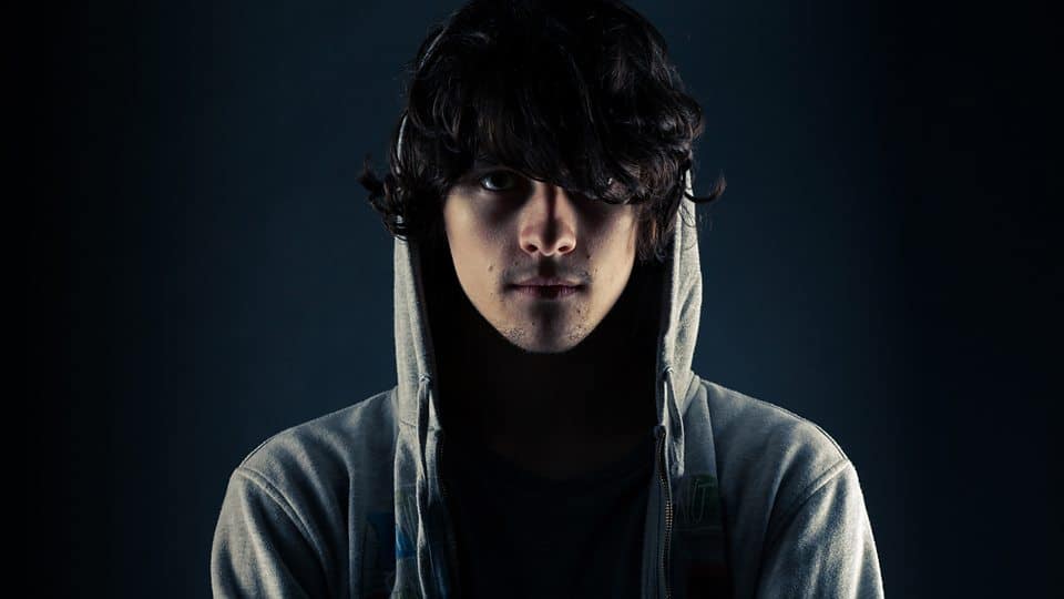 A young man in a hoodie looking at a Virtual Riot inspired dark background, while working on his FLP.