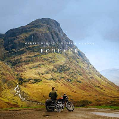 A man on a motorcycle in front of a mountain, listening to Martin Garrix.