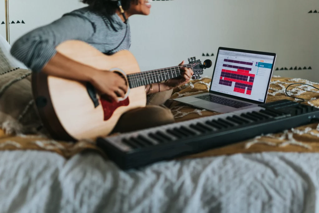 image showing a person playing a nylon guitar while using a laptop that displays a music visualization or music editing software