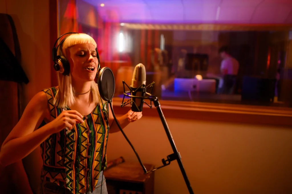 Vocalist singing upbeat tune, recording session in music studio.
